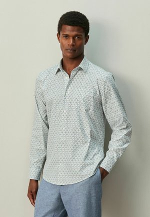 Cămașă cu nasturi și mâneci lungi, de culoare albastru deschis, cu un model decorativ. Are guler și tiv curbat. Asortată cu pantaloni gri deschis.