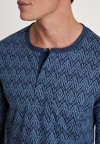 Navy button-up shirt met een geometrisch patroon in lichtblauw, met een ronde halslijn, een enkele borstzak en een zachte textuur.