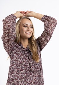 Bluză burgundy cu mânecă lungă, imprimeu floral, guler cu șnur și mâneci ample. Material ușor, cu o textură moale.