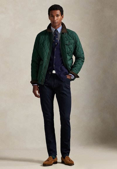 Grønn vattert jakke med brun krage, lagvis over en marineblå cardigan og stripete skjorte, kombinert med mørke jeans og brune loafers.