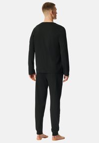 Zwarte set met lange mouwen en broek, gemaakt van zachte stof. Ontspannen pasvorm met rechte mouwen en manchetten. Minimalistisch ontwerp zonder zichtbare logo's.