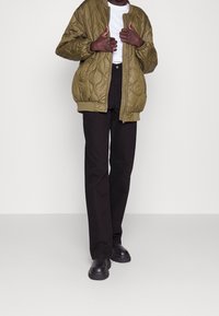 Pikowana bomberka w oliwkowej zieleni z zamkiem błyskawicznym, ściągaczami przy mankietach, w połączeniu z czarnymi spodniami o prostych nogawkach i masywnymi czarnymi butami.