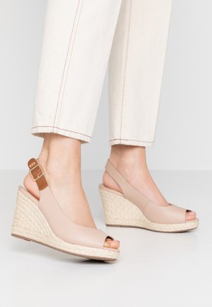 Sandales compensées beige à bout ouvert avec talons tressés et brides à boucle marron portées avec un pantalon de couleur crème.