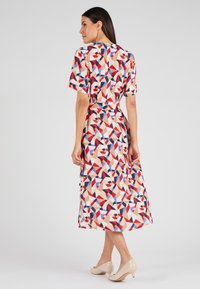 Multikleurige geometrische print jurk van lichtgewicht stof. Heeft korte mouwen, een ceintuur in de taille en een midi-lengte. Gecombineerd met naakte hakken.