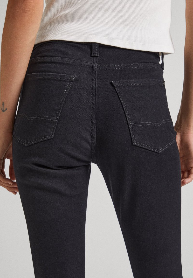 Schwarze Denim-Jeans mit einer taillierten Passform, mittelhoher Taille und zwei Gesäßtaschen mit kontrastierenden Nähten. Glatte Textur sichtbar.