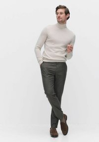 Lichtbeige coltrui, aansluitende snit. Donkergrijze geblokte broek met zakken. Bruine schoenen met een gestructureerde afwerking.