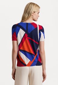 Short-sleeve knit top with a multicolored geometric pattern in red, blue, navy, and cream. Features a round neckline and ribbed edges.