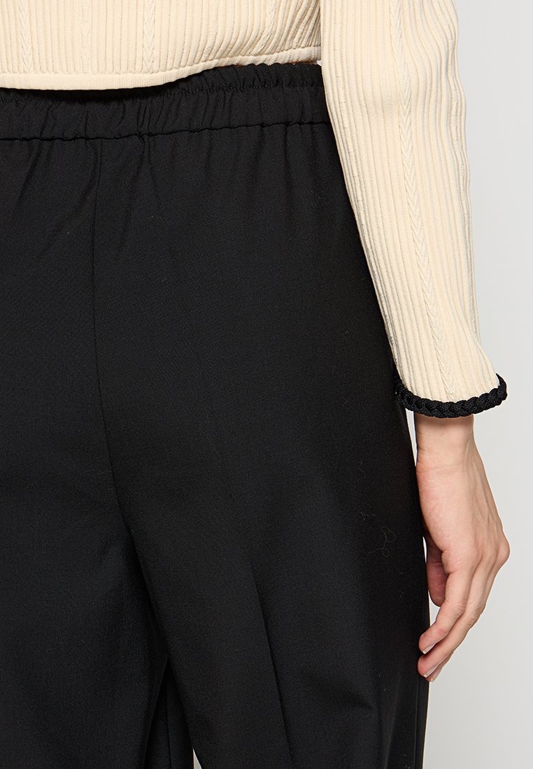 Romige geribde top met een aansluitende pasvorm en zwarte elastische broek. De broek heeft een gladde textuur en een losse pasvorm met een eenvoudige zoom.