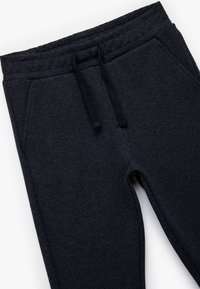 Mørkeblå joggers lavet af tekstureret stof med et herringbone-mønster, der har et elastisk liv med snoretræk. To sidelommer.
