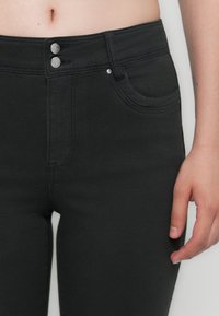 Melni denim džinsi ar augstu jostasvietu, kas aprīkoti ar diviem metāla pogu aizdari, priekšējiem kabatām un gludu, elastīgu tekstūru.