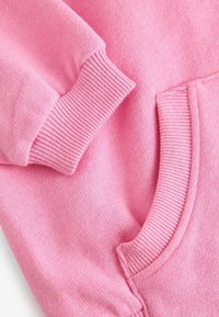 Sweatshirt rose avec des poignets et un ourlet côtelés, texture douce et poche kangourou. Le tissu semble chaud et léger.