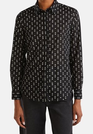 Chemise noire à manches longues avec motif losange blanc portée avec un pantalon noir, montrée du cou aux hanches.