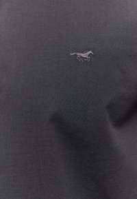 Camisa polo de tela negra con un pequeño logo bordado de un caballo gris en la parte superior izquierda. Textura suave con un acabado liso.