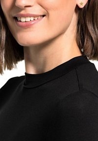 Top nero aderente con colletto alto. La modella indossa orecchini a forma di stella dorati. Sono visibili un tessuto liscio e dettagli di cucitura ben curati.