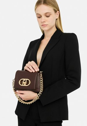 Borsa a tracolla in pelle marrone con texture trapuntata, tracolla in oro e chiusura con logo. Il modello indossa un blazer nero mentre tiene la borsa.