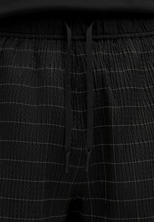 Pantaloni con vita elastica nera in tessuto testurizzato, caratterizzati da strisce bianche orizzontali e cordini neri in vita, che offrono un design casual.