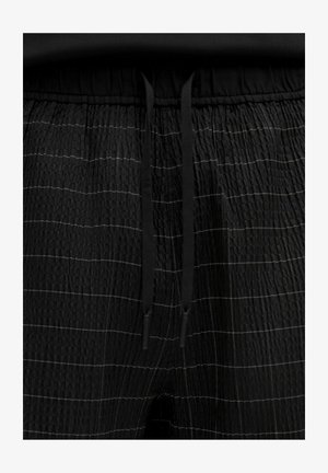 Černé kalhoty s elastickým pasem a texturovanou tkaninou, které mají horizontální bílé pruhy a černé šňůrky v pase, což zajišťuje ležérní design.