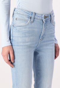 Jeans de mezclilla azul claro con corte ajustado, que cuentan con cremallera, cinco bolsillos y un ligero desvanecimiento. La tela tiene una textura suave.