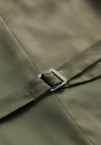Zeleni materijal s rebrastom teksturom, koji sadrži metalnu srebrnu kopču na remenu. Materijal je gladak i pomalo sjajan.
