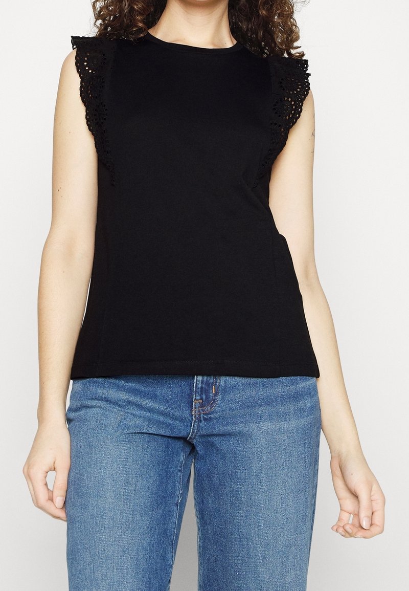 Sort ærmeløs top med blondedetaljer på skuldrene, med rund halsudskæring og tætsiddende pasform. Båret sammen med blå denimjeans.
