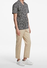 Camicetta a maniche corte a righe bianche e nere, design con bottoni, abbinata a pantaloni beige e sneakers bianche.