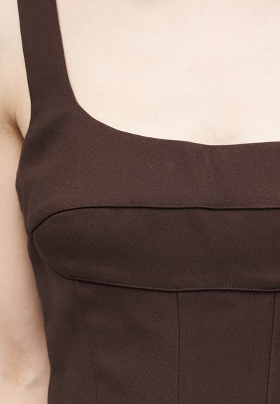 Κοντινό πλάνο ενός ατόμου που φοράει αμάνικο σκούρο καφέ φόρεμα με τετράγωνη λαιμόκοψη, εφαρμοστά ραφές και υφή υφάσματος.