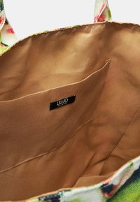 Borsa a spalla in tela con motivo floreale. L'interno presenta una foderatura in tessuto beige e una tasca a sbalzo. Etichetta del marchio visibile all'interno.