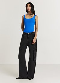 Body azzurro aderente con scollo quadrato abbinato a pantaloni cargo neri a vita alta con dettaglio a campana, dotati di tasche laterali e texture.