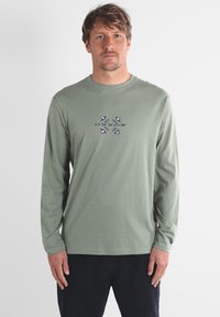 T-shirt à manches longues en coton vert avec un col rond et un design graphique bleu et violet centré sur le devant.