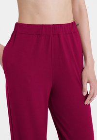 Pantaloni magenta, morbidi e di taglio ampio. Presentano un ampio cinturino elastico in vita e tasche laterali per maggiore comodità.
