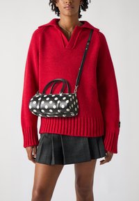 Red knitted sweater with a v-neck and ribbed cuffs, paired with a black and white polka dot handbag featuring rounded handles and a shoulder strap.