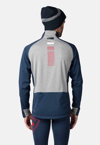 Marinblå och grå sportjacka med en randig detalj på baksidan, figurnära design och dragkedja i halsen. Tillsammans med en marinblå mössa.