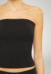Top nero senza spalline realizzato in tessuto elasticizzato, con un design aderente, bordi senza cuciture e una texture liscia. Non ci sono motivi o dettagli presenti.
