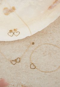 Goldschmuckset mit herzförmigen Ohrringen, einer Halskette mit zwei miteinander verbundenen Herzen und einem Armband mit einem einzelnen Herzanhänger.