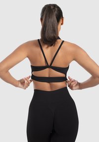 Top deportivo negro corto con diseño de espalda entrecruzada, hecho de tejido elástico. Combinado con leggins negros de cintura alta, que presentan una textura acanalada.