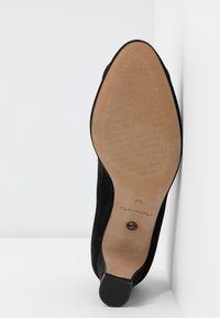 Chaussure à talon haut en suède noir présentée debout, montrant une semelle beige avec une prise texturée et une indication de taille "37" près du talon.