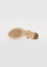 Beige høyhelte sandaler med såle med rillestruktur, har et bredt stroppe-design og firkantet hæl. Merkingen er synlig på innersålen.