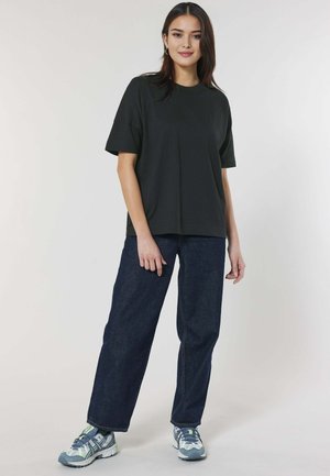 T-shirt noire à manches courtes associé à un jeans large bleu foncé et des baskets bleu-gris avec des accents verts. Design simple et coupe décontractée.
