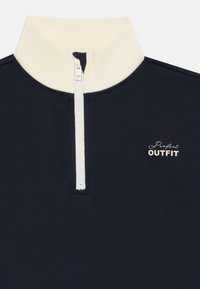 Mörkblå tröja med vit halvvipp och krämfärgad ståkrage, med texten "Perfect OUTFIT" på bröstet.