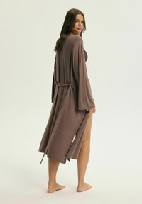 Długa, otwarta brązowa szata z miękkiego materiału, związywana w talii. Ma szerokie rękawy i boczny rozcięcie, noszona na ciemną bluzkę.