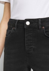 Jeans in denim nero con vita alta, dotati di chiusura a bottone metallico, tasche anteriori e tessuto leggermente testurizzato.