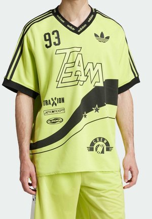 Muž v jasně žlutém sportovním dresu Adidas se černými pruhy, textem "TEAM", číslem 93 a různými logy a grafikou.