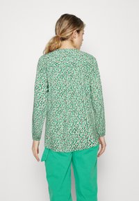 Lange mouwen blouse in groen met een bladdessin, lichte stof, gathered mouwen en een relaxte pasvorm, gecombineerd met groene cargobroeken.