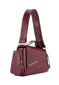 Burgundská kožená kabelka so štruktúrovaným tvarom, nastaviteľným ramenným popruhom, striebornými prvkami a prednou kapsou. Na boku je embosované logo "EXPATRIE".