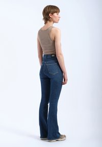 Fitted, tan ribbed tank top paired with high-waisted, dark blue flared jeans with two back pockets and a branded waistband. Brown sneakers.