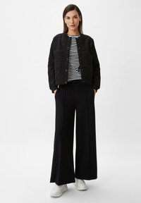 Quilted black jacket with snap buttons over a black-and-white striped shirt, paired with wide-leg black trousers and white sneakers.