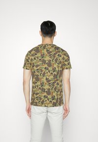 Krátký rukáv tričko v maskáčovém vzoru se zelenými, hnědými a béžovými odstíny; vyrobeno z bavlny; volný střih; kulatý výstřih.