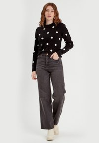 Zwarte trui met witte stippen, gecombineerd met hoogpszit, wijdvallende grijze jeans en crèmekleurige enkellaarsjes. Soepele gebreide textuur, casual ontwerp.