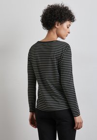 Schwarzes Langarmshirt mit dünnen weißen Streifen, aus weichem Material, abgerundetem Saum und lässiger Passform, das die Rückansicht und die Details der Schulternaht zeigt.
