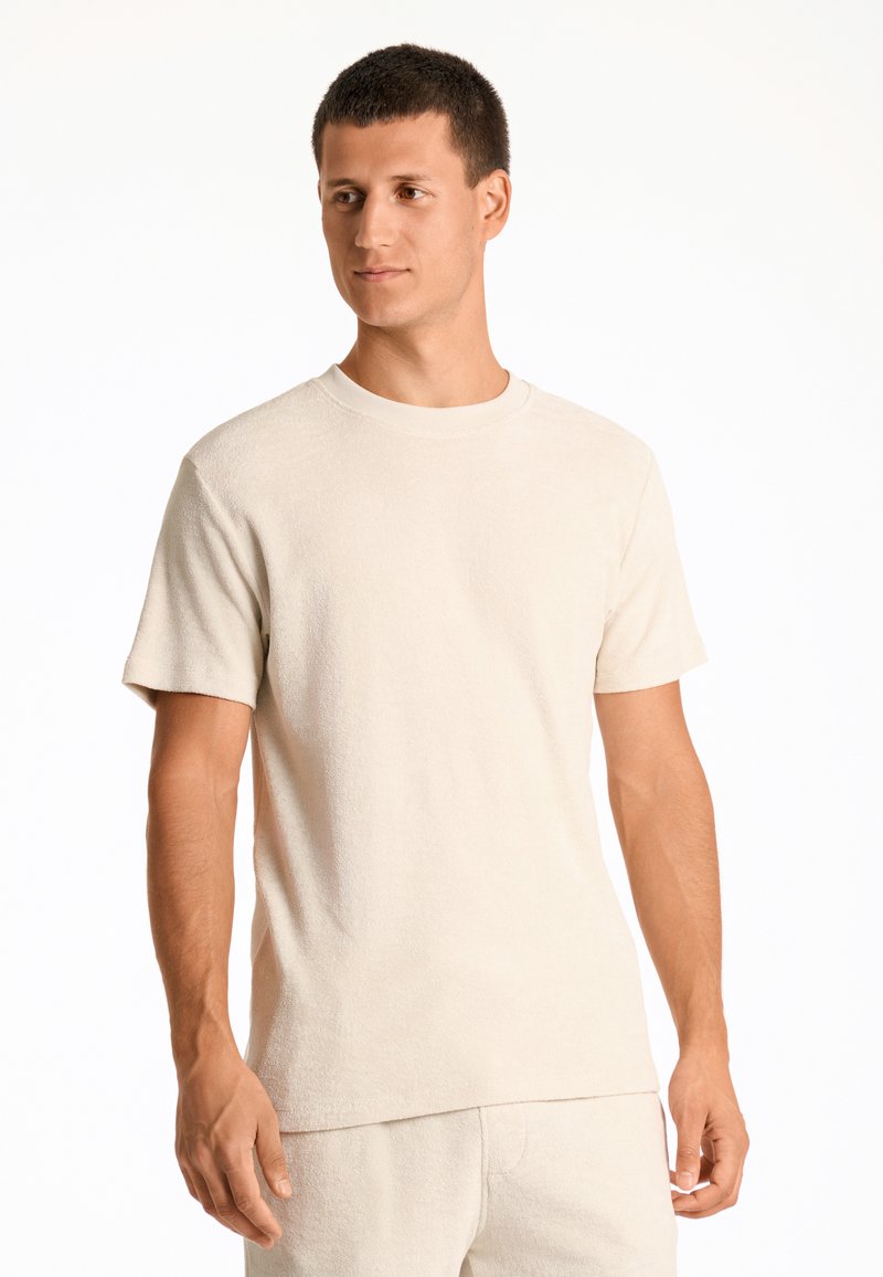Camiseta de manga corta beige hecha de tela texturizada. Presenta un escote redondo y un corte relajado. Combinada con pantalones beige a juego.
